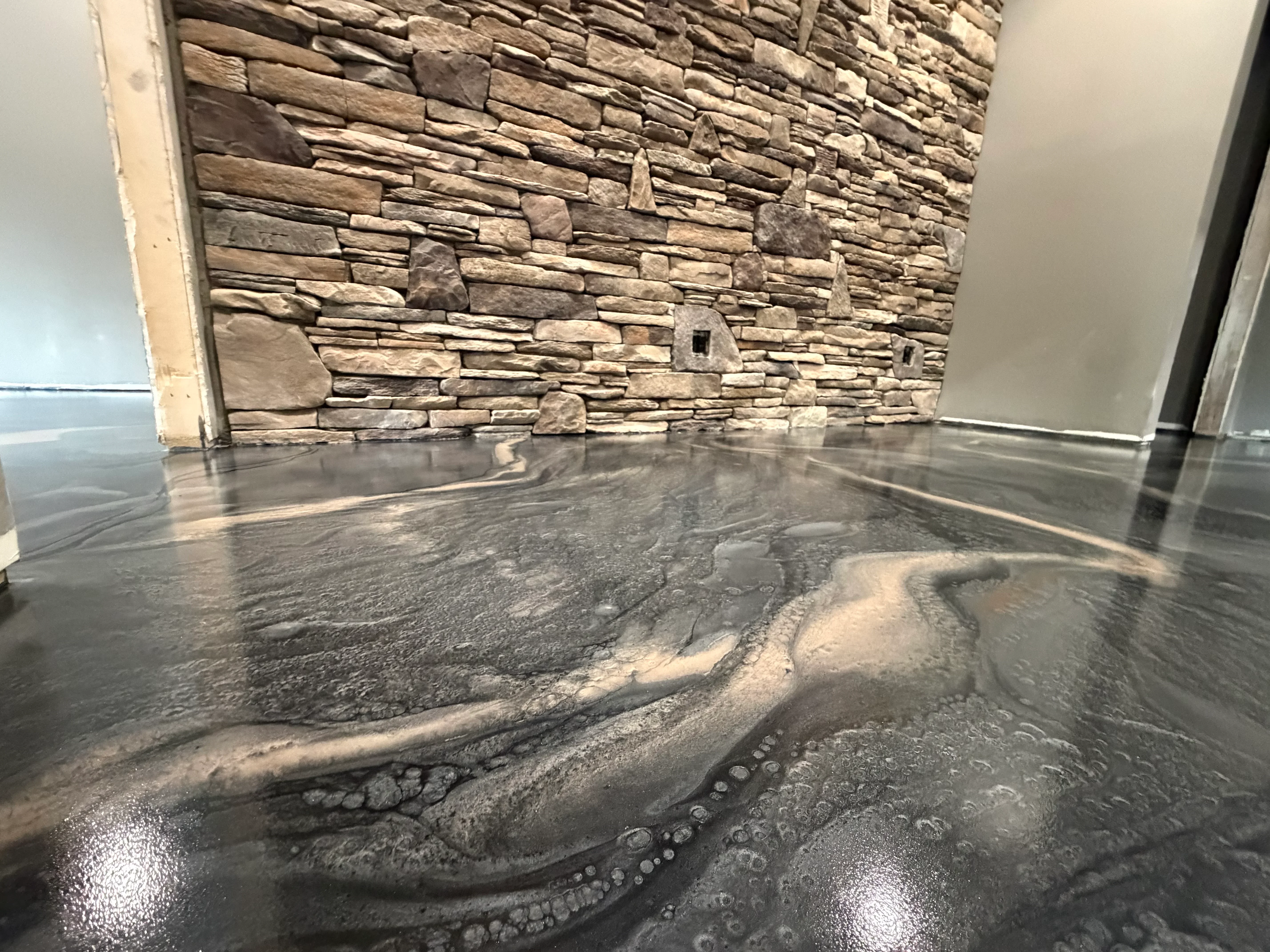 Metallic gray epoxy floor with swirl patterns and stacked stone wall backdrop