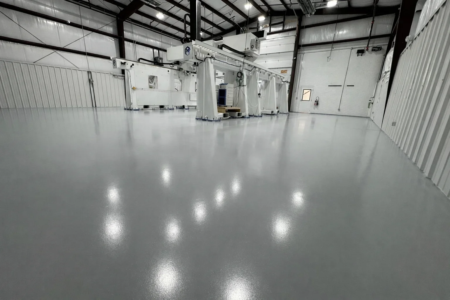 Polished gray epoxy floor in industrial warehouse with metal frame structure and overhead lighting