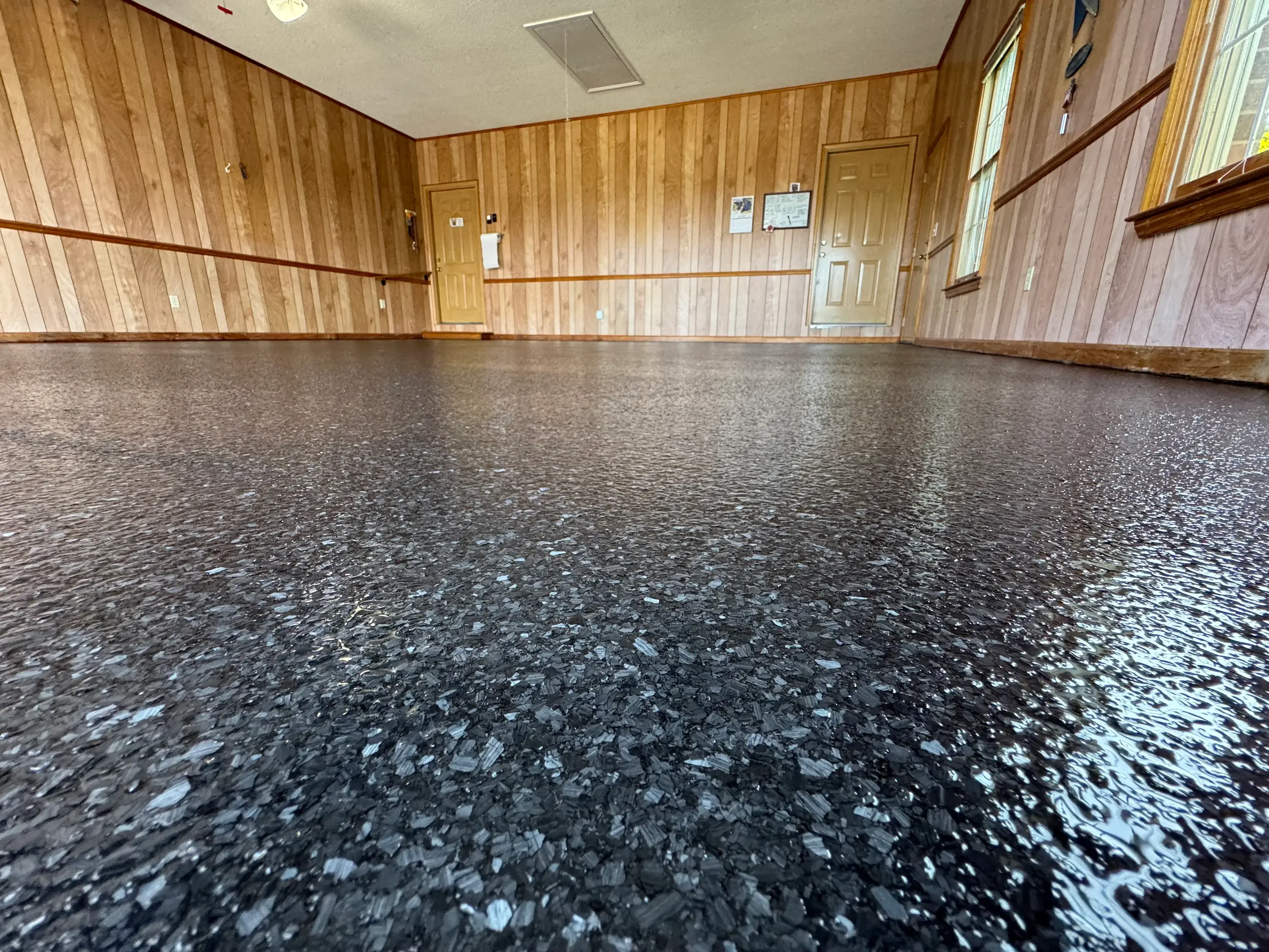 Dark epoxy floor with white and gray flakes in wood-paneled interior space