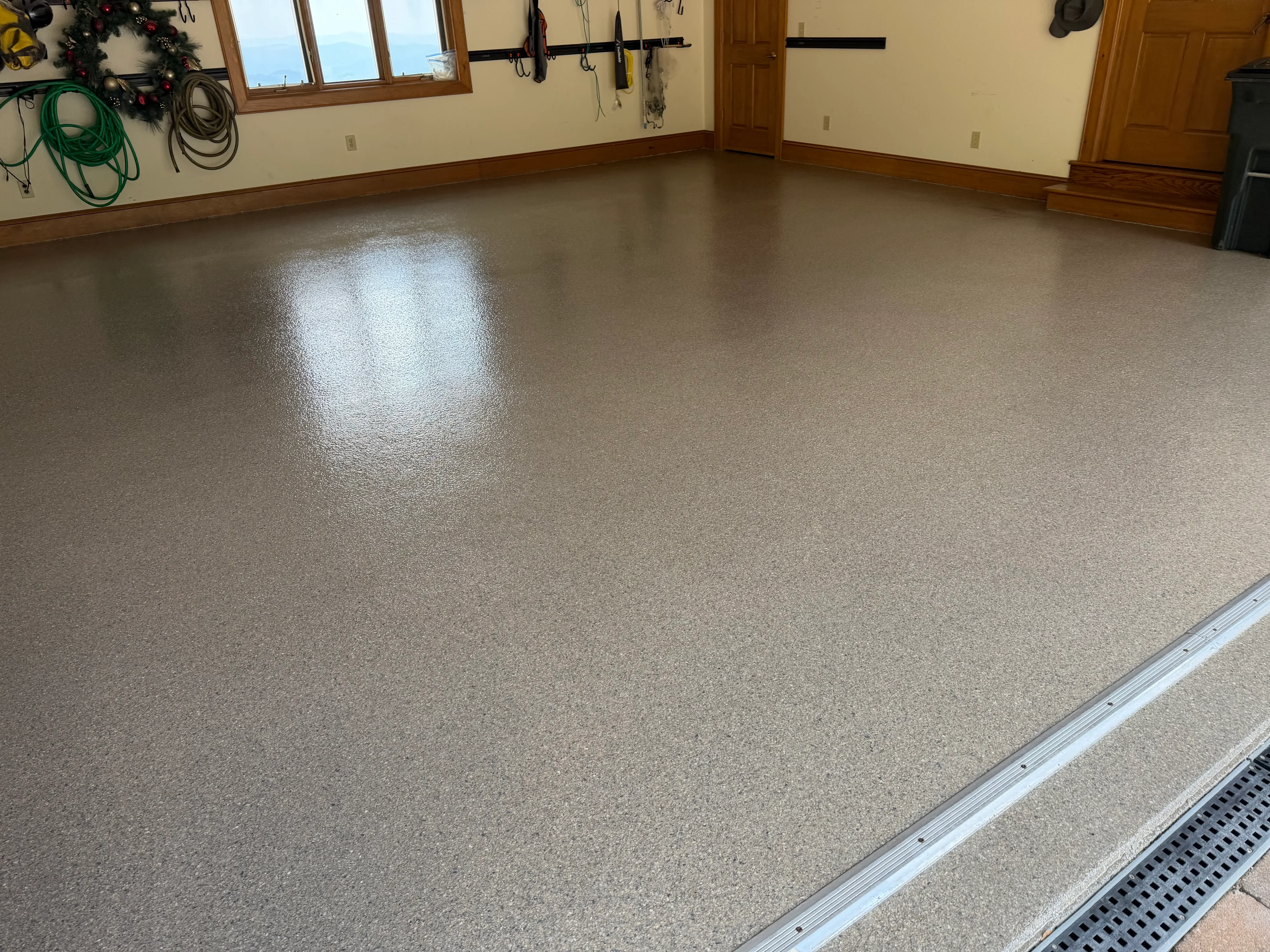 Speckled tan epoxy-coated garage floor with glossy finish and aluminum threshold trim