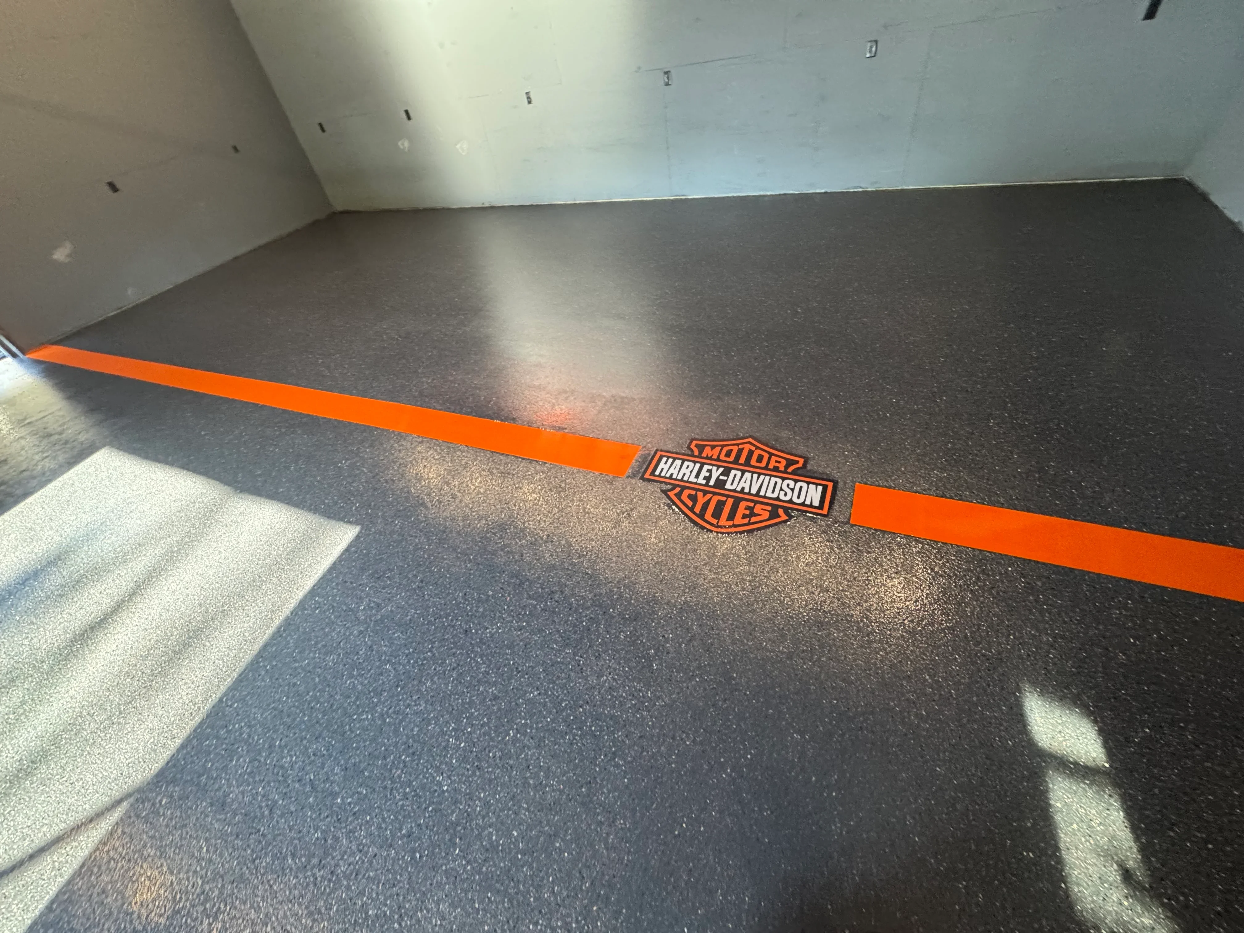 Dark epoxy garage floor with orange stripe and Harley-Davidson logo inlay